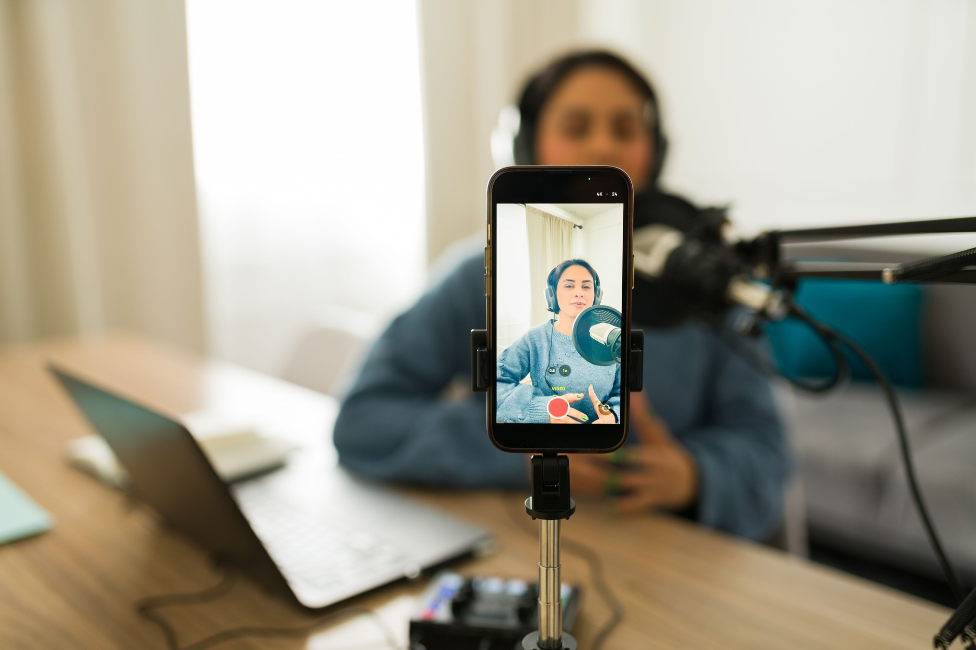 Female podcaster recording audio and live streaming content using smartphone in home studio setting